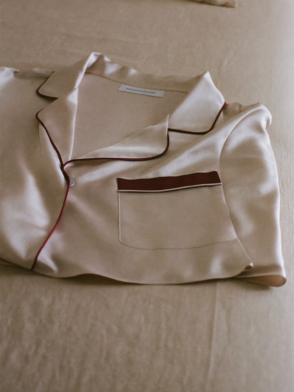 Champagne silk pajamas with burgundy piping on linen bedding